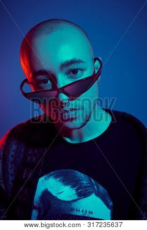 Studio Shot Of A Young Tattoed Bald Man Posing Against A Blue Background. 90s Style.