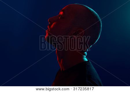 Studio Shot Of A Young Tattoed Bald Man Posing Against A Blue Background. 90s Style.