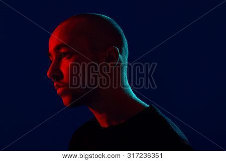 Studio Shot Of A Young Tattoed Bald Man Posing Against A Blue Background. 90s Style.