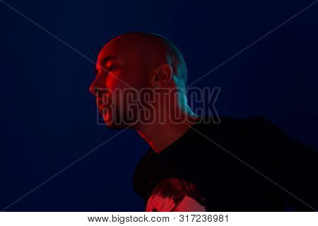 Studio Shot Of A Young Tattoed Bald Man Posing Against A Blue Background. 90s Style.