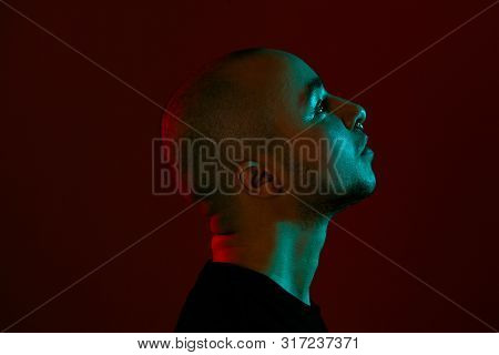 Studio Shot Of A Young Tattoed Bald Man Posing Against A Red Background. 90s Style.