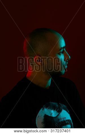 Studio Shot Of A Young Tattoed Bald Man Posing Against A Red Background. 90s Style.