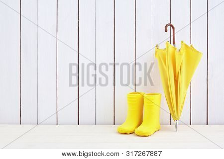 A Pair Of Yellow Rain Boots And A Umbrella On White Wooden Background