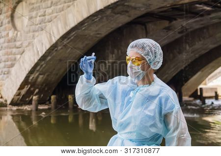 Female Ecologist Or Epidemiologist Anxiously Examines A Test Tube With Water From A City River