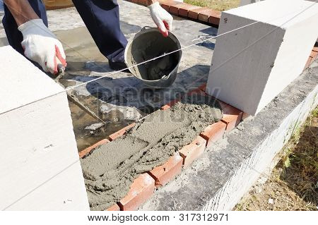 The Worker Begins The First Row Of Masonry Construction In White Gas Blocks.
