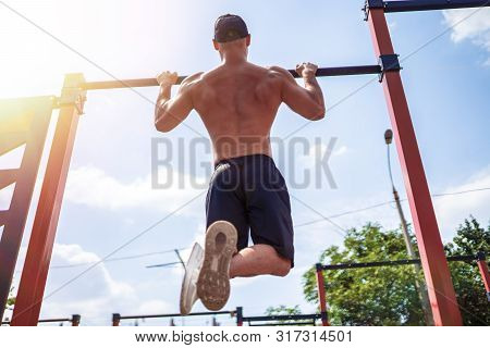 Brutal Athletic Man Making Pull-up Exercises On A Crossbar At Outdoor Streeet Gym. Back View.