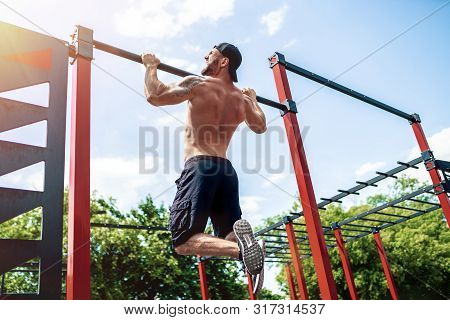 Brutal Athletic Man Making Pull-up Exercises On A Crossbar At Outdoor Streeet Gym. Back View.
