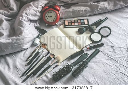 Make Up Cosmetic And Brushes, Alarm Clock And Blank Page Notepad On The Blanket On The Bed Backgroun