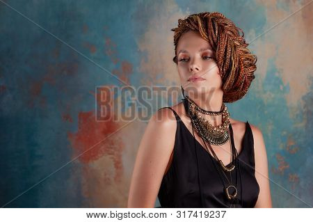 Southern Spices. A Beautiful Young Blue-eyed Woman With Afrocos And Large Ornaments Against A Textur