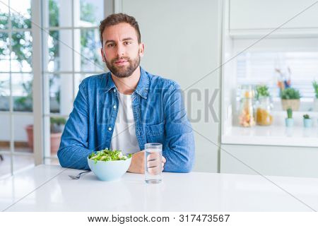 Handsome man eating fresh healthy salad with serious expression on face. Simple and natural looking at the camera.