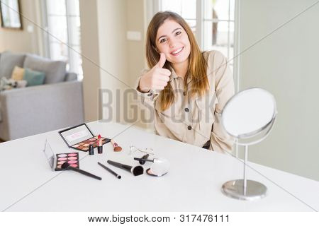 Beautiful young woman using make up cosmetics doing happy thumbs up gesture with hand. Approving expression looking at the camera showing success.