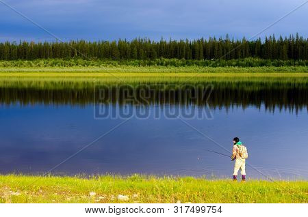 Yakut Girl-tourist Angler With A Backpack Pulls Out A Spinning Lure Out Of The Water North Of The Vi