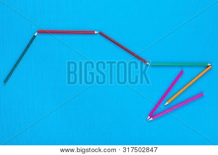 A Bunch Of Crayons Forming An Arrow On An Blue Background, Shot From Above.