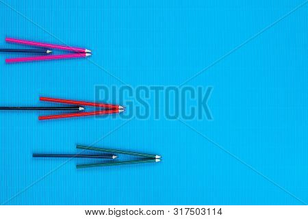 A Bunch Of Crayons Forming Arrows On An Blue Background, Shot From Above, Arranged To The Left.