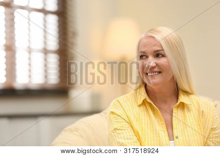 Portrait Of Happy Mature Woman Sitting In Papasan Chair At Home