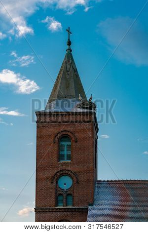 Church In Guelpe, Germany With Two Storks Breeding On The Clock Tower Roof