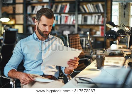 Let Me See. Young And Handsome Bearded Man In Formal Wear Examining Documents While Sitting In His M