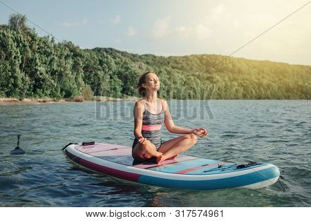 Middle Age Caucasian Woman Practicing Yoga On Paddle Sup Surfboard At Sunset. Female Stretching Doin