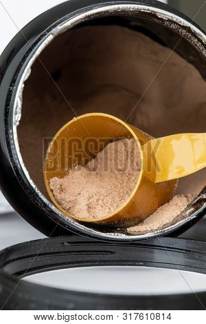 Plastic Measuring Spoon And Heap Of Brown Chocolate Protein Powder. Sport Nutrition Concept.