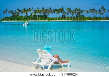Women In A Blue Hat Lies On A White Lounger On The Beach In The Maldives, Looks At A Beautiful Parad