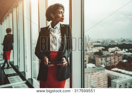 An African-american Woman Entrepreneur A Digital Tablet Is Leaning Against A Panoramic Window Of An 
