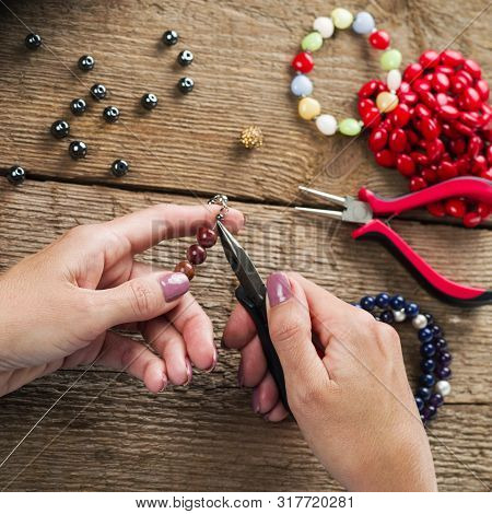 Jewelry Making. Making Bracelet Of Colorful Beads. Female Hands With A Tool On A Rough Wooden Table.
