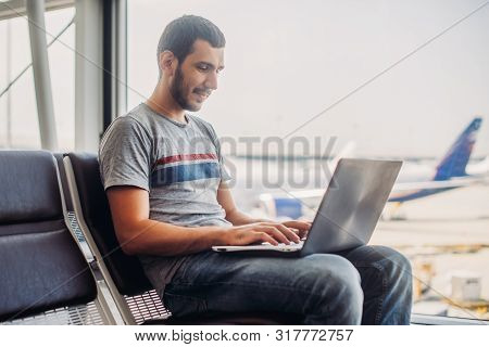 Young Man Using Laptop In Airport Terminal