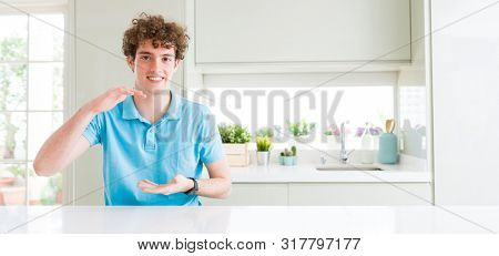 Wide shot of young handsome man at home gesturing with hands showing big and large size sign, measure symbol. Smiling looking at the camera. Measuring concept.
