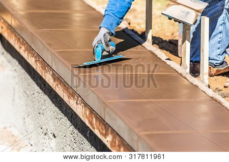 Construction Worker Using Trowel On Wet Cement Forming Coping Around New Pool.
