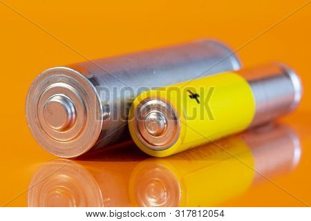 Single Used Aa And Single Aaa Alkaline Battery Are Seen On A Reflective Orange Surface. Closeup Side
