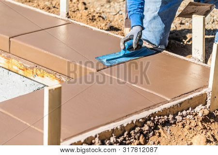 Construction Worker Using Trowel On Wet Cement Forming Coping Around New Pool.