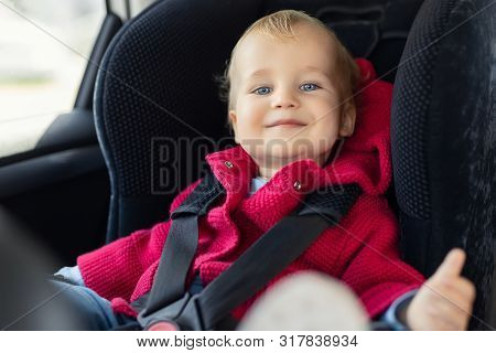 Cute Caucasian Toodler Boy Sitting In Child Safety Seat In Car During Road Trip. Adorable Baby Smili
