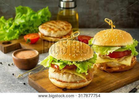 Two Homemade Burgers With Cutlet Of Chicken Meat, Melted Cheese, Tomatoes And Bacon On A Wooden Boar