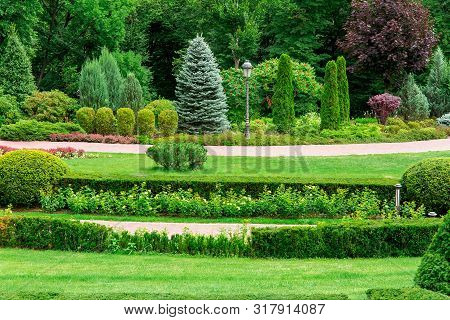 Empty Park With Walking Paths For Walks Among Landscape Design With Bushes And Trees On A Summer Day