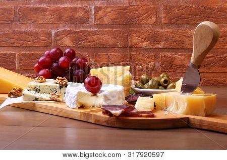 Assortment Of Cheese With Fruits, Grapes, Nuts And Cheese Knife On A Wooden Serving Tray.