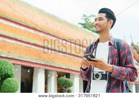 Handsome Asian Man Tourist Walking And Looking Smart Phone At Wat Suthat Thepwararam Ratchaworawihan
