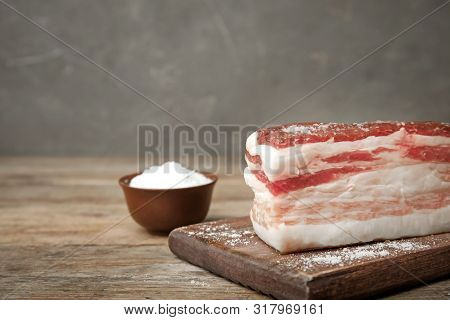 Board With Bacon And Salt On Wooden Table. Space For Text