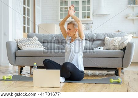 Senior Woman Spending Time At Home, Online Training In Living Room. Exercising With Laptop Watching 
