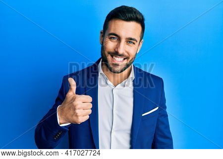 Young hispanic businessman wearing business jacket doing happy thumbs up gesture with hand. approving expression looking at the camera showing success. 