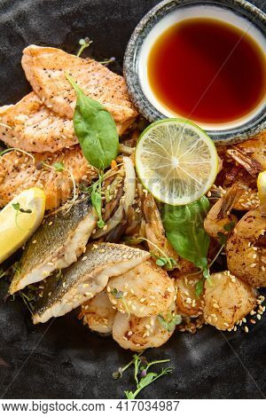 Teppanyaki Style Seafood - Grilled Mixed Seafood with Soy Sauce and Vegetables. Japanese Teppanyaki Salmon Steak, Shrimp, Scallop and Fish Fillet garnished with lemon and green salad. Top view