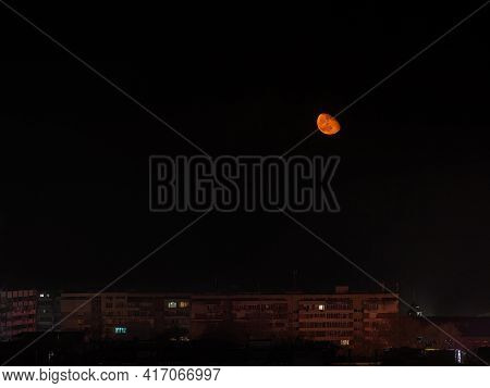 Rising Large Orange Moon Low In The Sky Over Multi-storey Residential Buildings. View Of The Sleepin