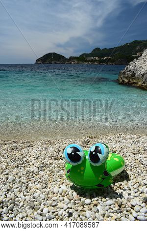Green Inflatable Frog On A Deserted Pebble Beach