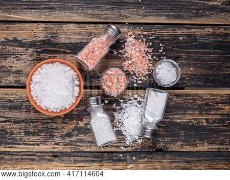 Some Sea Salt And Himalayan Salt In Bowls And Coming Out Of Salt Shakers On Dark Wooden Background, 