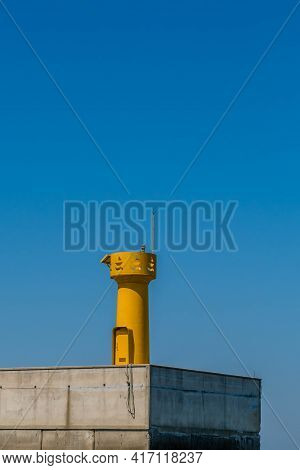 Yellow Lighthouse On End Of Concrete Pier With Clear Blue Sky In Background.