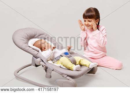 Beautiful Dark Haired Girl With Pigtails Sitting On Floor And Playing With Newborn Sistrer Lying In 