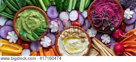 Narrow Close Up View Of Three Dips Surrounded By Fresh Cut Vegetables For Dipping.