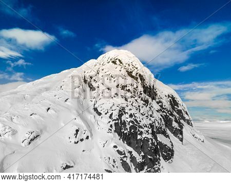 Panoramic View Of A Snow Capped Mountain Peak With Clouds And Blue Skies. Mount Bitihorn In Norway.