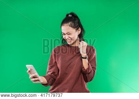 Beautiful Woman Holding And Look Handphone With Happiness Expression While Raising One Hand And Maki