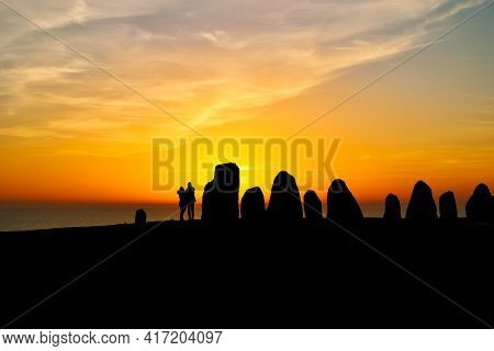 Colorful Partially Cloudy Sky At Sunset Over The Sea. Silhouettes Of Ales Stenar Megalithic Monument