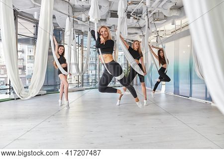 Group Of Female Are Doing Fly Yoga Exercises In Fitness Training White Gym Loft Classroom. Intense F